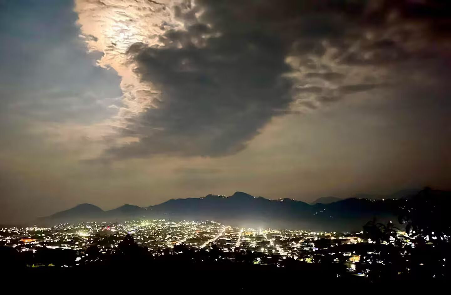 A nighttime cityscape with a mountain range in the background.