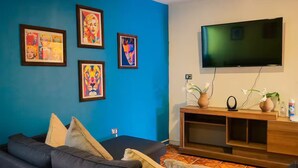 A living room with a blue wall, a large flat-screen TV, a dark-colored sofa, and framed artwork. - Quiet Family Apartment 2 Blocks from Zacatlán Downtown (Zacatlán)