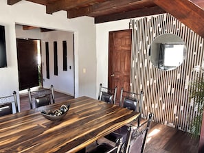 Un espace repas comprenant une longue table en bois, des chaises et un panneau décoratif mural.