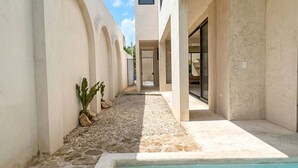 A modern pool area with a clear blue pool, surrounded by a concrete deck and a pathway leading to a building entrance. - Jungle Villa + Private Studio w/ Rooftop Access | 2BR + Studio | Sleeps 6 (Tulum)