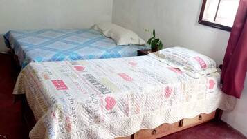 Ein Schlafzimmer mit zwei Betten, einem kleinen Tisch, einer Zimmerpflanze und einem Fenster mit Vorhängen.