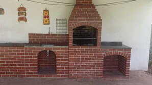 Ein gemauerter Außenofen mit Schornstein, einem Metallrost und einem hängenden Schild mit Text.