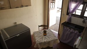 Ein kleines Zimmer mit Tisch, Stuhl, Zimmerpflanze, Schrank und einem Fenster mit Vorhängen.