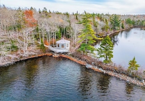Une cabane au bord d’une rivière paisible, entourée d’arbres.