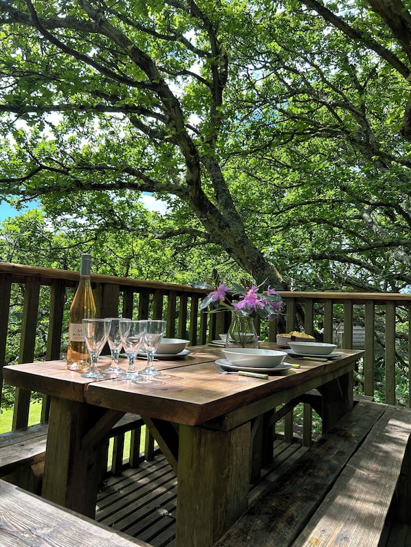 Eine Holzterrasse mit Esstisch, umgeben von üppigem Grün.