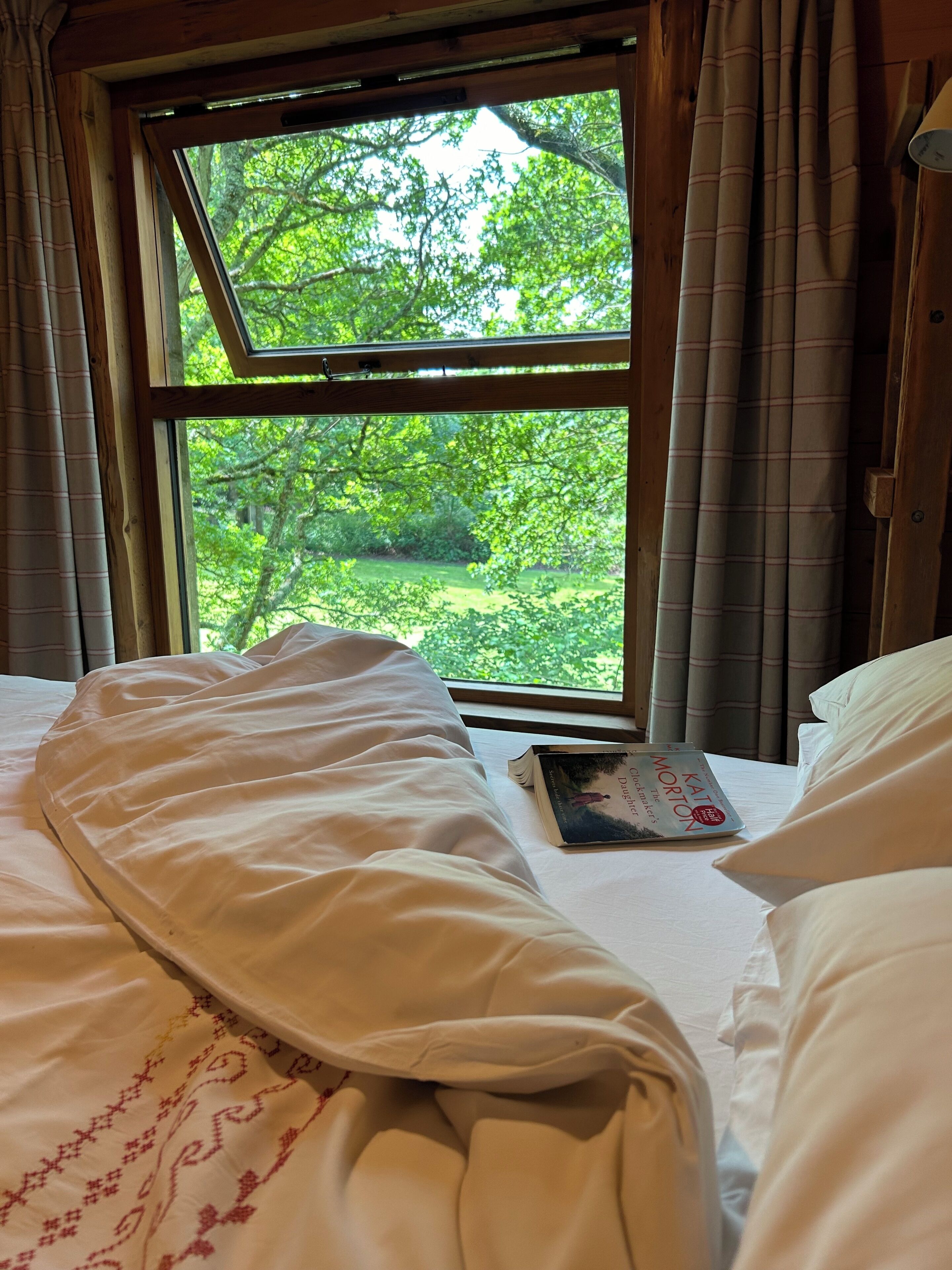 A bedroom with a large window, a bed, and a book on the bed.