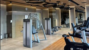 A modern gym with cardio machines, weightlifting equipment, and a wooden ceiling. - Cozy Retreat King Suite (Mandaluyong City)