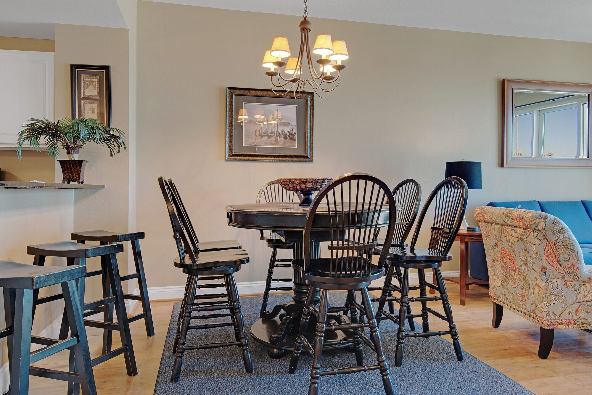 A dining area with a round table, six chairs, a chandelier, framed pictures, and a potted plant.