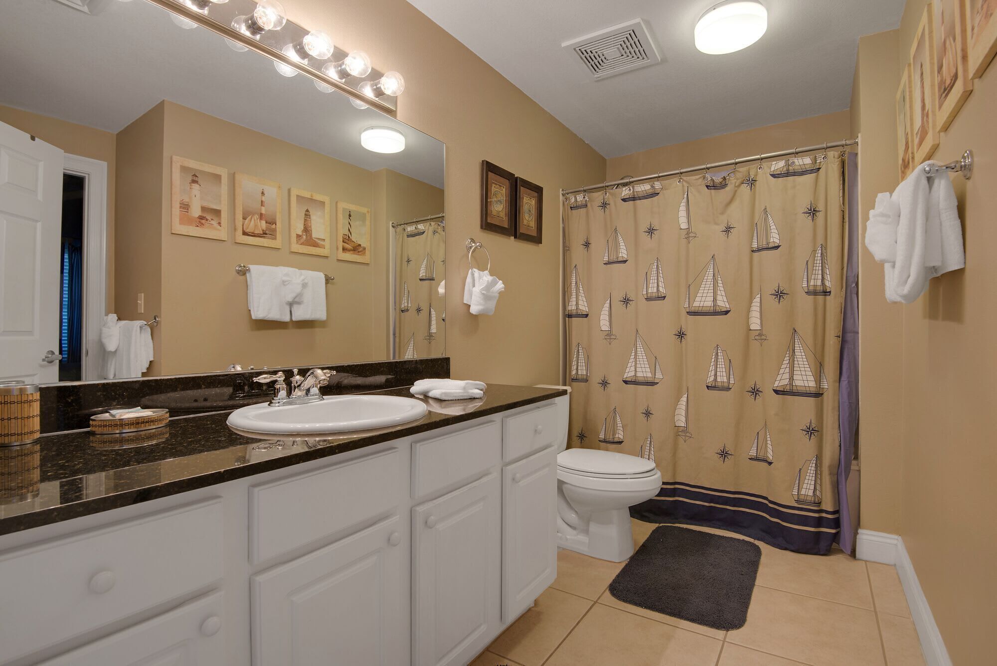 Une salle de bain équipée d’un meuble-lavabo, d’un évier, d’un miroir et d’un rideau de douche sur le thème de la marine.