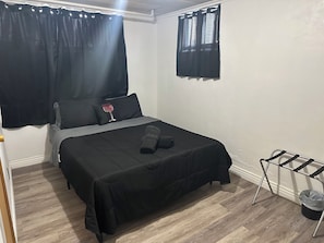 Ein Schlafzimmer mit einem Bett, schwarzen Vorhängen, einem Fenster, einem kleinen Tisch mit einer Dekoration und einem Wäscheständer.