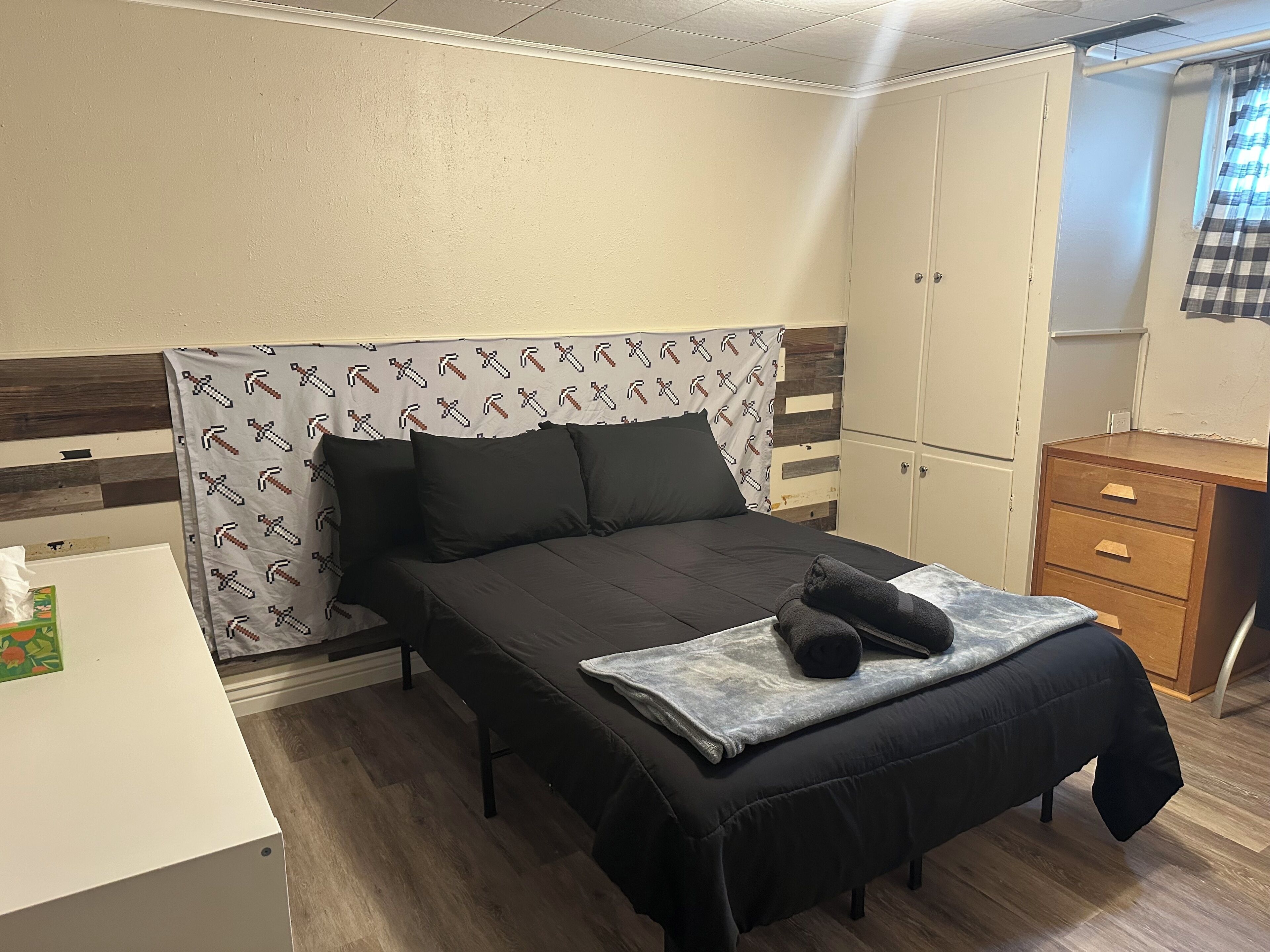 A bedroom with a bed, a bench, a desk, a wardrobe, and a window with curtains.