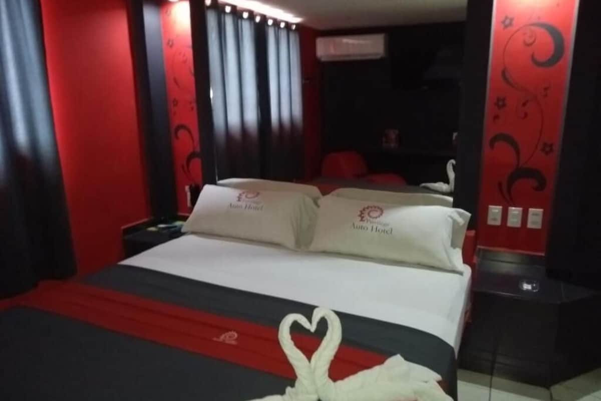 Una habitación de hotel con cama, decoración en tonos rojo y negro, y una toalla con forma de corazón sobre la cama.