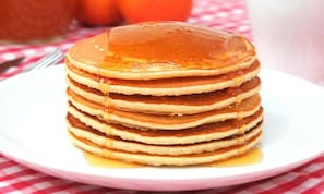 Una pila de tortitas con almíbar sobre un plato blanco.