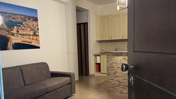 A living room with a sofa, a kitchen with stone backsplash, and a view of a cityscape through a window.