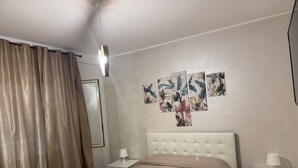 A bedroom with a bed, two bedside tables, a ceiling light, a window with curtains, and a wall with a floral mural.