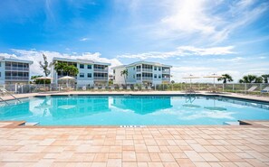 Una piscina con borde de baldosas, rodeada de edificios con balcones y palmeras.