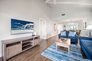 A living room with a wooden entertainment unit, a blue sofa, and a coffee table. - Sanibel Beach Club 2 Beachfront 2BR Escape (Sanibel)
