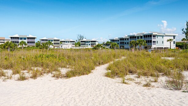 Un hôtel situé en bord de mer, composé de bâtiments à plusieurs étages, de sentiers sablonneux et d’une végétation clairsemée.