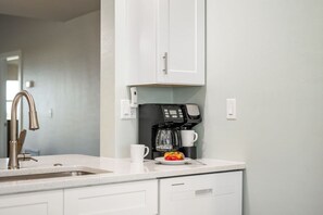 A kitchen with a coffee maker, a sink, and a plate with fruit. - Sanibel Beach Club 2 Beachfront 2BR Escape (Sanibel)