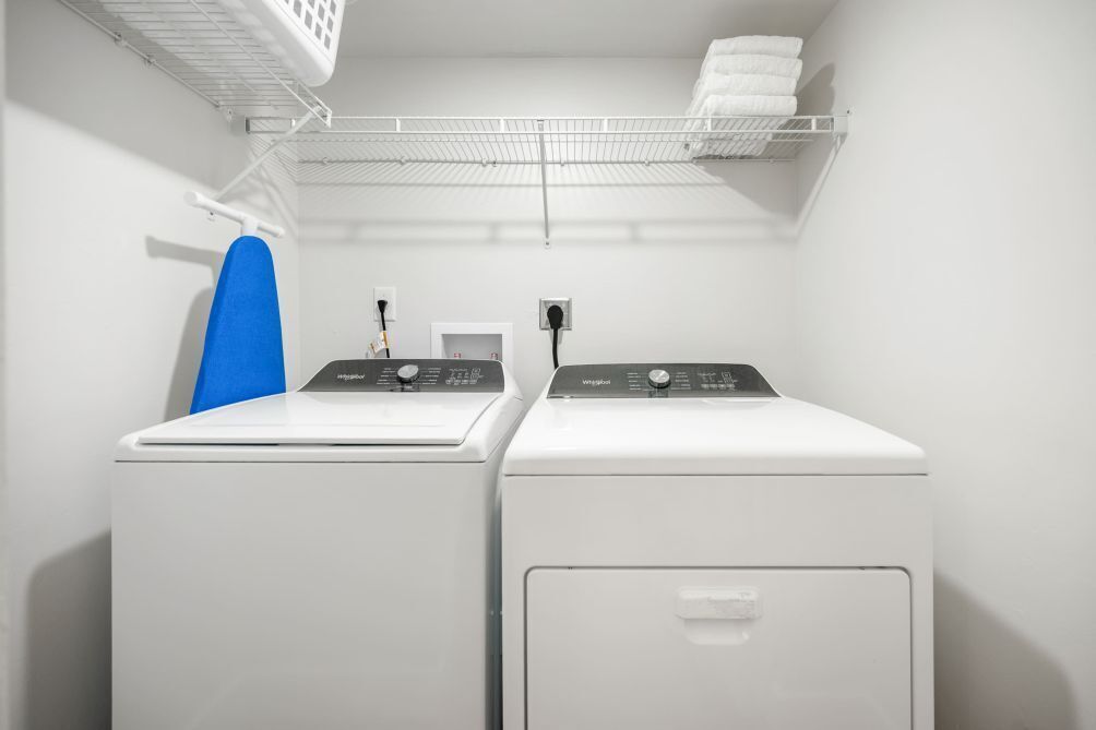 A laundry room with two front-loading washing machines, a blue ironing board, and a wall-mounted drying rack.
