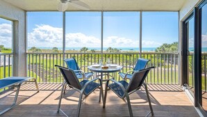 Un balcon avec une table et des chaises, un ventilateur de plafond et une vue sur l’océan.