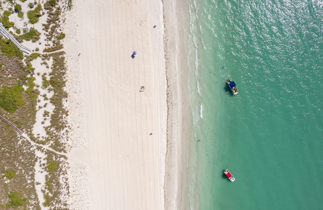 An aerial view of a beach with clear water, a sandy shore, and a few boats.