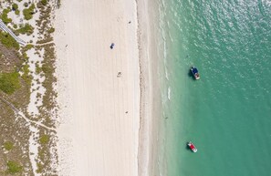 Vista aérea de una playa con agua cristalina, una orilla arenosa y algunas embarcaciones.