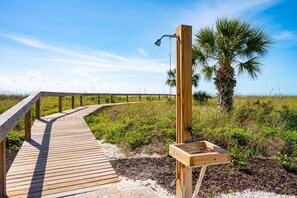 A wooden boardwalk leading to a wooden structure with a water fountain and a palm tree in the background. - Sanibel Beach Club 2 Beachfront 2BR Escape (Sanibel)