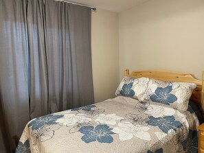A bed with floral bedding, a wooden headboard, and a grey curtain.