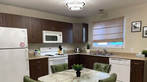 A kitchen with a white refrigerator, stove, microwave, and dishwasher. There is a dining table with chairs and a potted plant. - Tranquil Candle Lake Townhouse Backing the 5th Green (Candle Lake)
