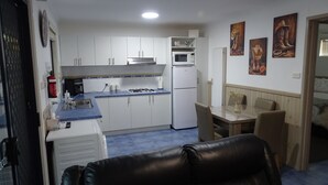 Cocina compacta con armarios blancos, microondas y estufa a gas. Cuenta con un comedor con mesa y sillas, y una sala de estar con sofá de cuero.