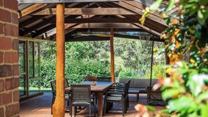 Eine Terrasse im Freien mit einem Holztisch und -stühlen, umgeben von Pflastersteinen und einer Glasverkleidung.