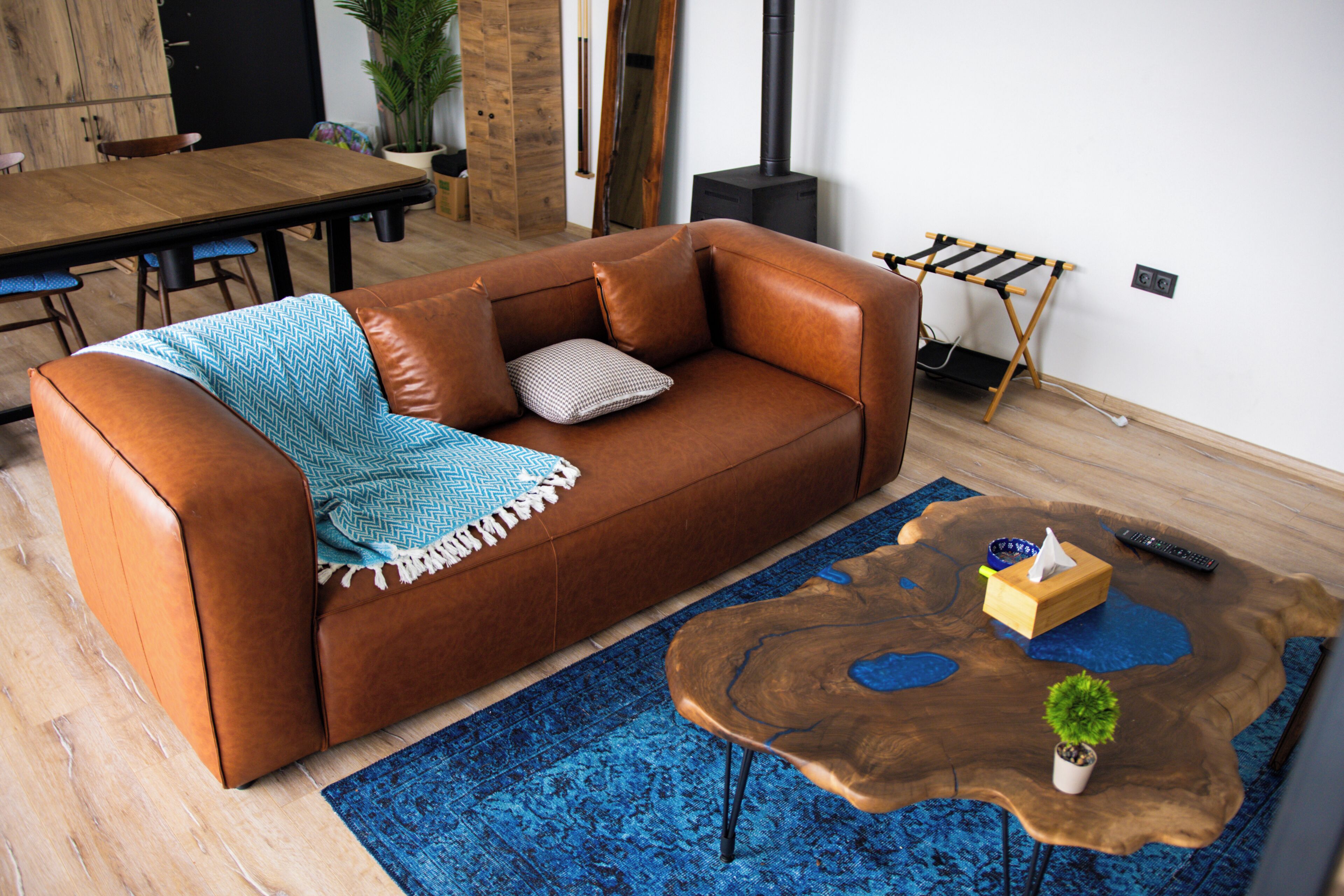A brown leather sofa with a blue patterned throw blanket, a wooden coffee table with a plant, and a blue patterned rug.