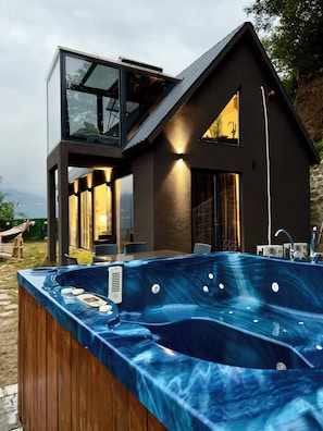 A modern house with a glass balcony, a hot tub, and a dining area.