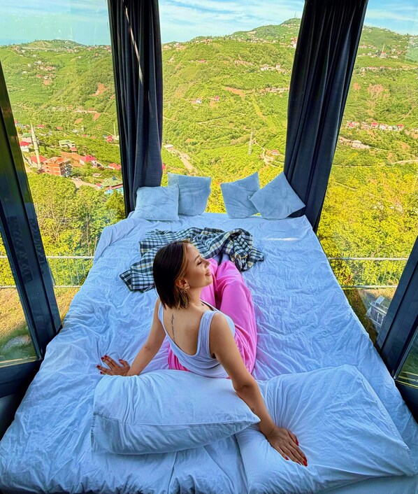 A bed with a view of a green landscape.