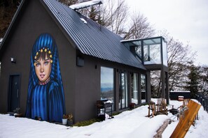 A modern building with a large mural on the side, a glass conservatory, and outdoor seating.