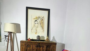 A room with a wooden floor, a colorful striped sofa, a small wooden table with a book, a lamp, and a framed artwork on the wall.
