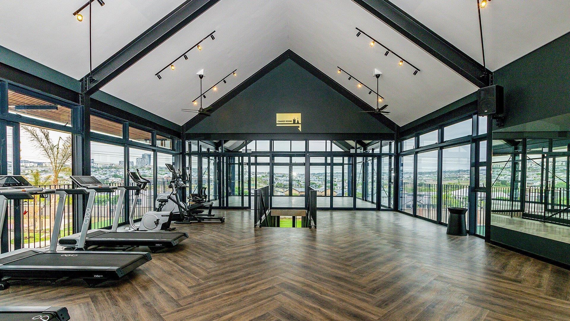 Ein geräumiges Fitnessstudio mit Trainingsgeräten, großen Fenstern und einer hohen Decke.