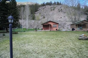 Eine kleine Holzhütte mit Veranda, Rasen und einer Hügelkulisse im Hintergrund.