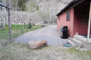 Ein Schotterweg führt zu einer roten Holzhütte mit einem schwarzen Grill davor.