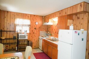 Eine kompakte Küche mit Holzwänden, einer Mikrowelle, einem Herd, einem Spülbecken und einem Kühlschrank.