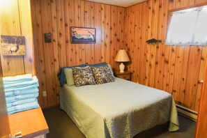Ein Zimmer mit Holzwänden, einem Bett mit grüner Bettdecke, einem Nachttisch mit Lampe und einem Willkommensschild.