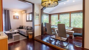 Una sala de estar moderna con un sofá, una mesa de comedor con sillas, una pequeña mesita auxiliar y un espejo grande que refleja la habitación.
