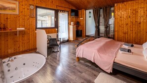 Una habitación con paneles de madera, una cama, una bañera, una silla y un televisor.