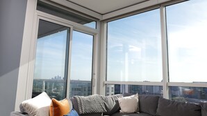 A modern living room with a large window, a gray sofa, and a city view. - Breathtaking views! Where Luxary meets comfort. 1-BR condo in charming Buckhead! (Atlanta)