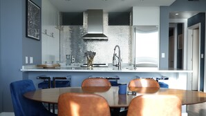 A modern kitchen with a central island, blue chairs, and a dining table. - Breathtaking views! Where Luxary meets comfort. 1-BR condo in charming Buckhead! (Atlanta)