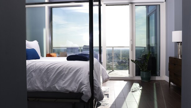 A bedroom with a large bed, a nightstand, a lamp, a potted plant, and a sliding glass door leading to a balcony. - Breathtaking views! Where Luxary meets comfort. 1-BR condo in charming Buckhead! (Atlanta)