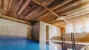 An indoor swimming pool with wooden ceiling beams, clear glass walls, and a visible pool ladder.
