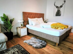 Un dormitorio con cama, mesitas de noche, lámpara, planta en maceta, alfombra y una obra de arte con ciervo en la pared.