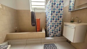 Un baño con bañera, cortina de ducha, lavamanos con espejo y toallero.